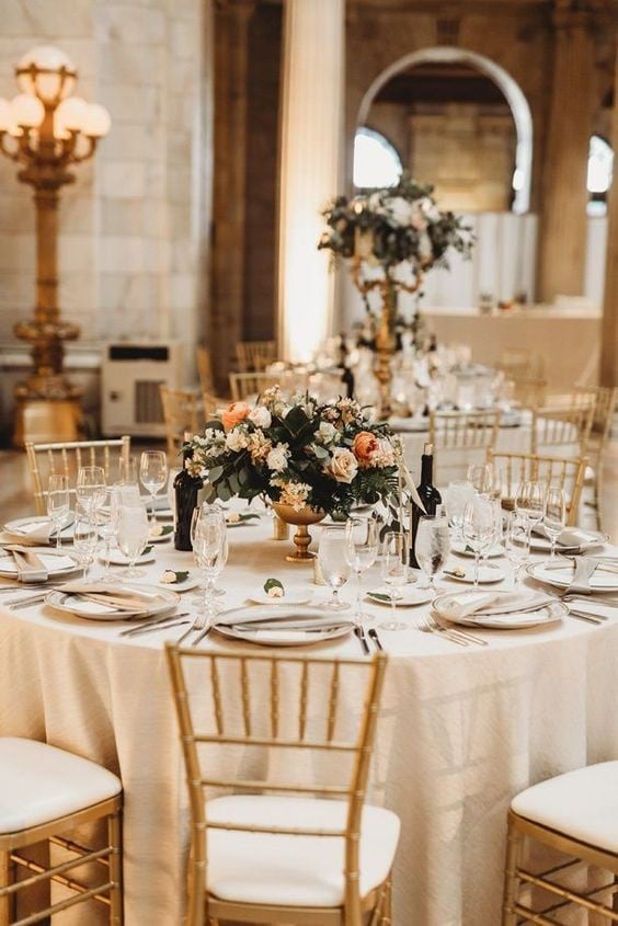 Elegant ballroom wedding reception decor with gold chairs, round tables and low peach wedding centerpieces |