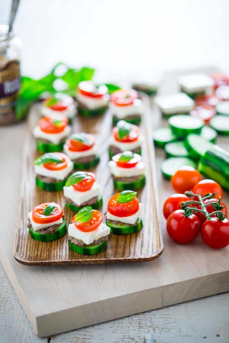 Check out this Greek salad cucumber party bites. The flavors of Greek salad in an easy one bite appetizer. It is no cook and comes together in minutes. Layer black olive pesto on cucumber slices. Top with a square of feta cheese, basil and a slice of tomato.